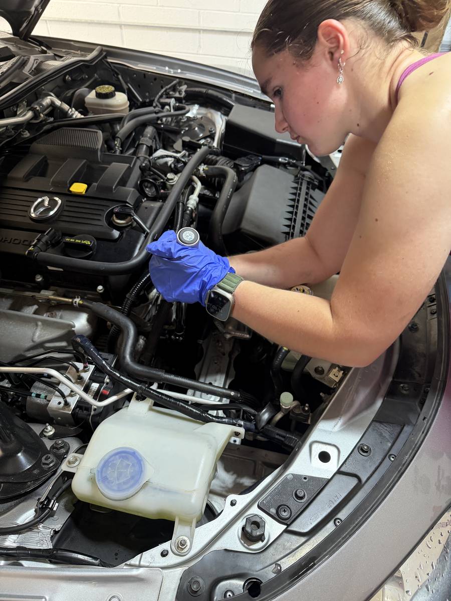 Holding the new aluminum power steering reservoir cap over the engine bay, ready for install